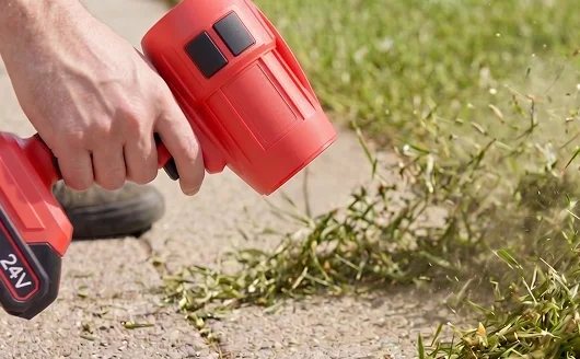 Blower aimed at grass clippings along a sidewalk.