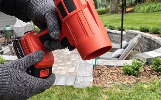Gloved hands holding the red blower near a patio.